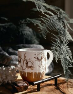 Künstlerisch gestaltete Tasse neben einem Farnzweig im Sonnenlicht: Selbstfürsorge und kleine Pausen im Alltag integrieren mit Vivio Karlsruhe.